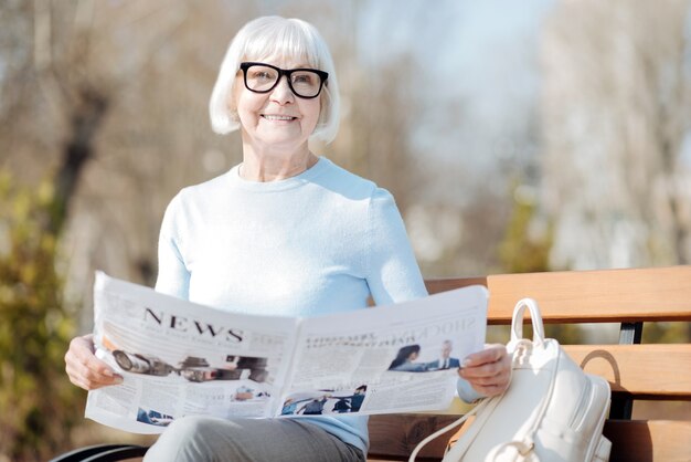 Photo wonderful news. alert aged woman reading a newspaper while sitting on the bench