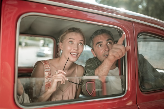 Прекрасный вид. Пораженная улыбающаяся супружеская пара, видя достопримечательности города и указывая на них, сидя на заднем сиденье машины.