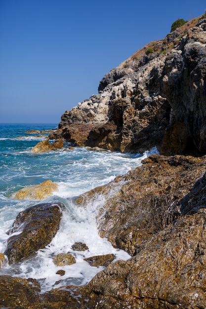 Wonderful views of the blue Mediterranean Sea. Sunny rocks, waves with foam and splashing water. The wave crashes into the rocks on the shore