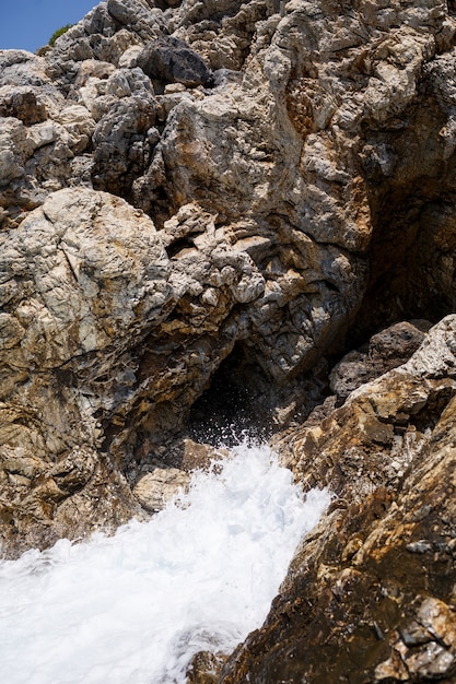 Wonderful views of the blue Mediterranean Sea. Sunny rocks, waves with foam and splashing water. The wave crashes into the rocks on the shore