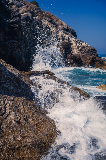 Wonderful views of the blue Mediterranean Sea Sunny rocks waves with foam and splashing water The wave crashes into the rocks on the shore