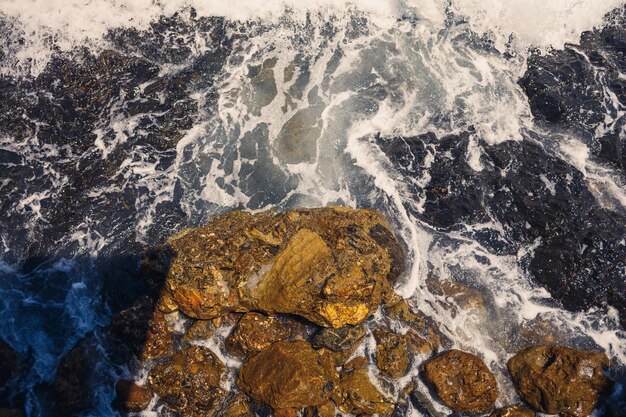 Wonderful views of the blue Mediterranean Sea Sunny rocks waves with foam and splashing water The wave crashes into the rocks on the shore