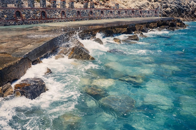 Wonderful views of the blue mediterranean sea sunny rocks waves\
with foam and splashing water the wave crashes into the rocks on\
the shore