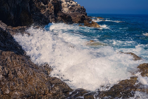 Wonderful views of the blue mediterranean sea sunny rocks waves\
with foam and splashing water the wave crashes into the rocks on\
the shore