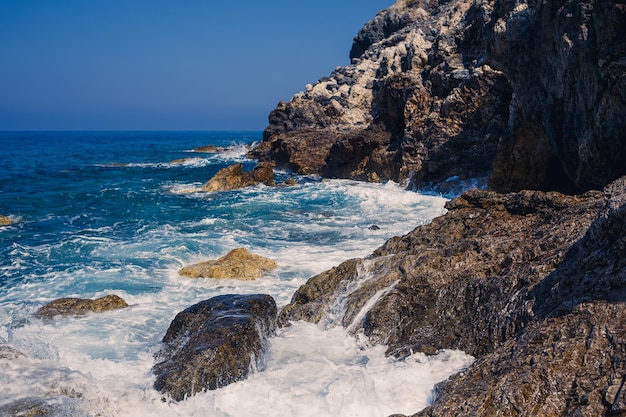 Wonderful views of the blue Mediterranean Sea Sunny rocks waves with foam and splashing water The wave crashes into the rocks on the shore