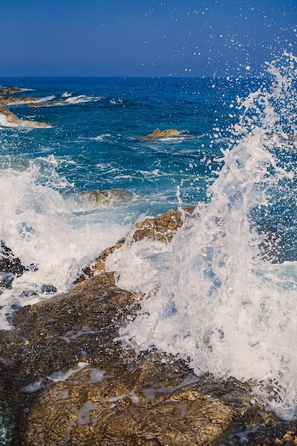 Wonderful views of the blue mediterranean sea sunny rocks waves\
with foam and splashing water the wave crashes into the rocks on\
the shore