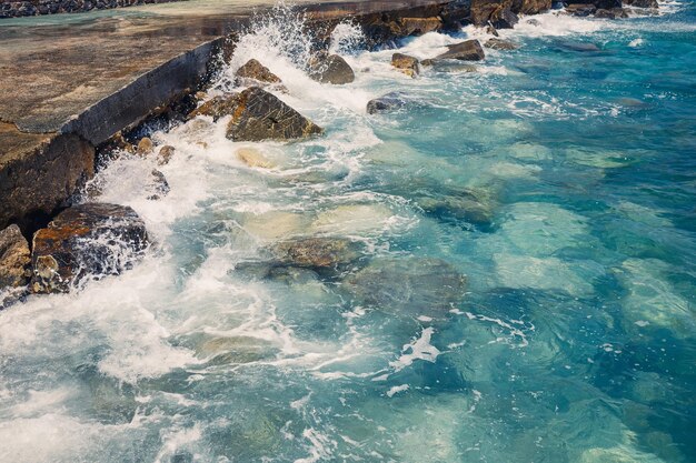 Wonderful views of the blue Mediterranean Sea Sunny rocks waves with foam and splashing water The wave crashes into the rocks on the shore