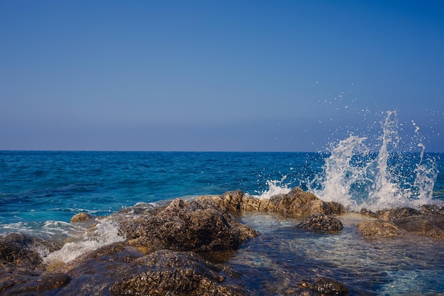 Wonderful views of the blue mediterranean sea sunny rocks waves\
with foam and splashing water the wave crashes into the rocks on\
the shore