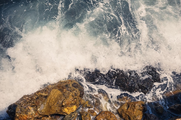 Wonderful views of the blue mediterranean sea sunny rocks waves\
with foam and splashing water the wave crashes into the rocks on\
the shore