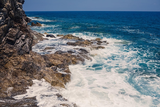 Wonderful views of the blue Mediterranean Sea Sunny rocks waves with foam and splashing water The wave crashes into the rocks on the shore