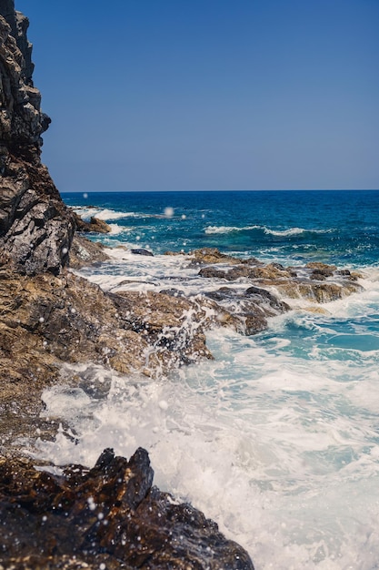 Wonderful views of the blue mediterranean sea sunny rocks waves\
with foam and splashing water the wave crashes into the rocks on\
the shore