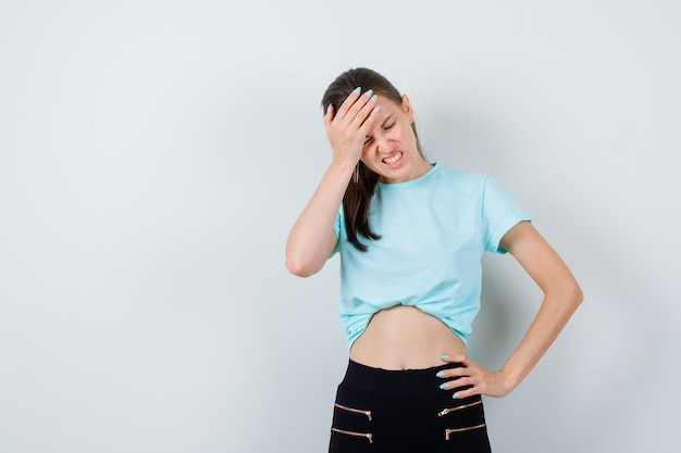 Meravigliosa donna in camicetta, pantaloni che tiene la mano sulla fronte e sembra pentita, vista frontale.