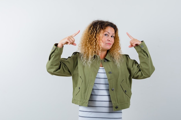 Wonderful woman pointing up in green jacket, shirt and looking confident . front view.