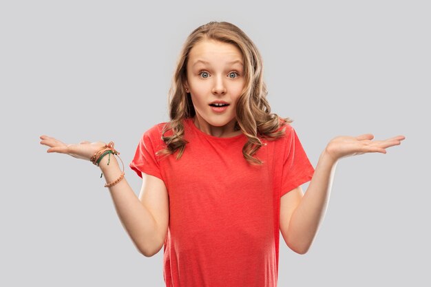 Photo wondering teenage girl in red tshirt shrugging