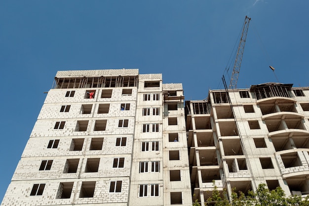 Woningbouw met meerdere verdiepingen in aanbouw en kraan op een achtergrond van blauwe lucht