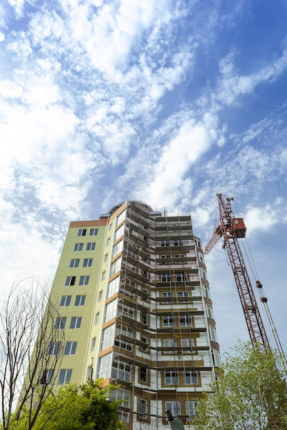 Foto woningbouw met meerdere verdiepingen in aanbouw en kraan op een achtergrond van blauwe lucht