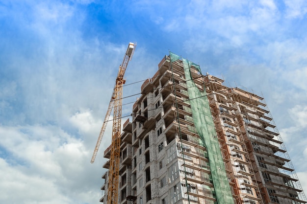 Woningbouw met meerdere verdiepingen in aanbouw en kraan op een achtergrond van blauwe lucht