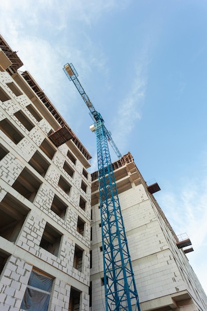 Woningbouw met meerdere verdiepingen in aanbouw en kraan op een achtergrond van blauwe lucht