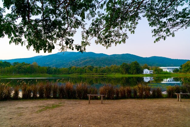 タイの森林に覆われた山と夕暮れの空とチェンマイの美しい湖のある木製のベンチ。
