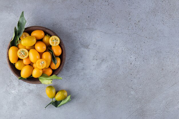 Wood bowl of fresh juicy kumquats on stone surface