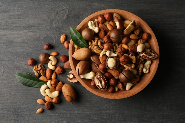 Wood bowl with different tasty nuts on gray wooden background