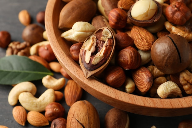 Wood bowl with different tasty nuts on gray wooden background