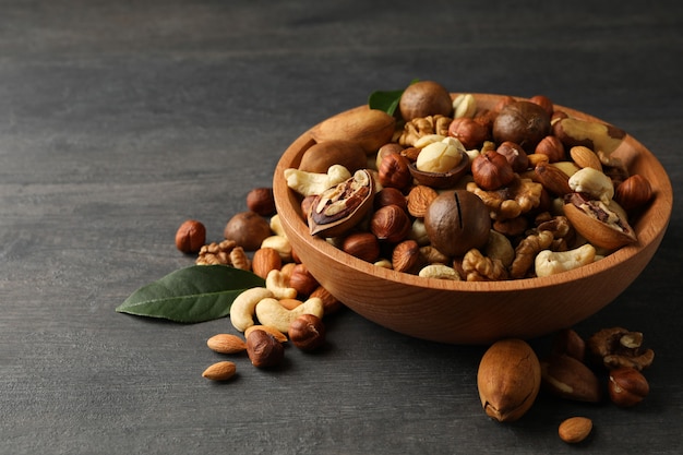 Wood bowl with different tasty nuts on gray wooden table