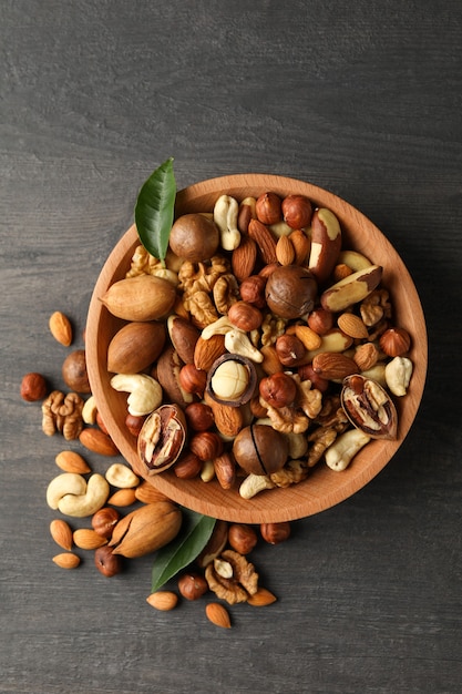 Wood bowl with different tasty nuts on gray wooden table