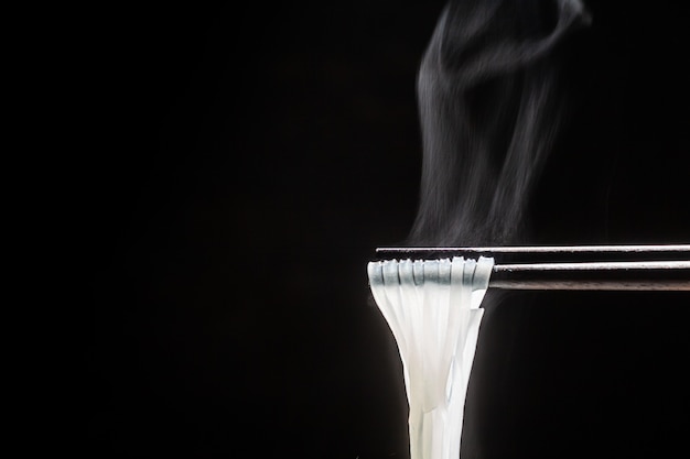 Wood chopsticks to pickup noodle with steam and smoke on black