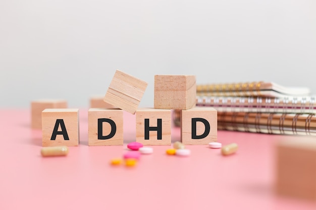 Photo wood cube block abbreviation of adhd with stethoscope and pills on pink table attention deficit hyperactivity disorder adhd concept