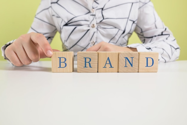 Wood cube block with word brand on wooden table brand building\
for success conceptwomen\'s hands holding cubes with the word\
brands