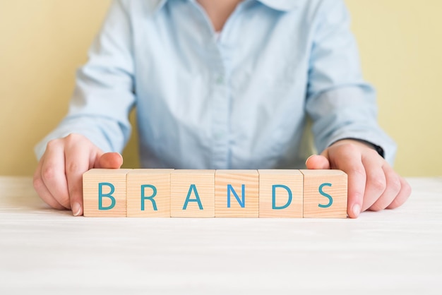 Wood cube block with word brand on wooden table brand building\
for success conceptwomens hands holding cubes with the word\
brands