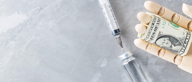 Wood hand with vial with syringe vaccine and one dollar on gray background