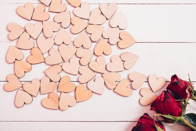 Cuori di legno e rose rosse su fondo di legno bianco