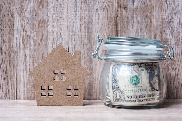 Wood house model and money glass jar, American dollar banknote.