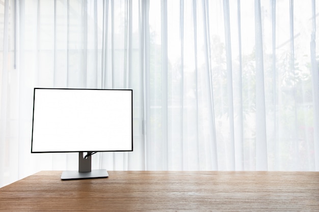 Wood office table with blank screen on monitor on curtain window at home. 