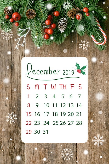 Фото Деревянная доска по вертикали с сосновыми листьями и шишками, шарами падуба, снегом и леденцом в рождественской концепции с календарем на 2019 год