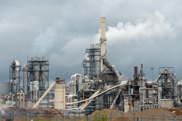 Wood processing plant against the background of gray clouds White toxic smoke comes out of factory chimneys Utopian landscape Environmental pollution An environmental disaster