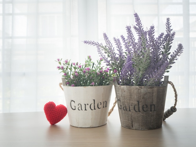 Wood table with beautiful flower and red heart shape sign on white curtain window backgrou