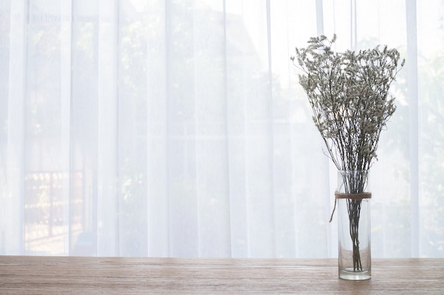 wood table with dried gypsophila flower on white curtain backdrop. 