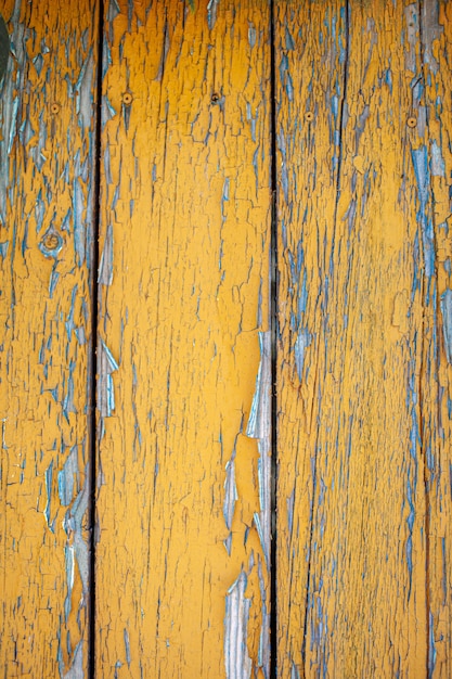 Wood texture with yellow flaked paint. Peeling paint on weathered wood. Old cracked paint pattern on rusty background. Chapped paint on an old wooden surface