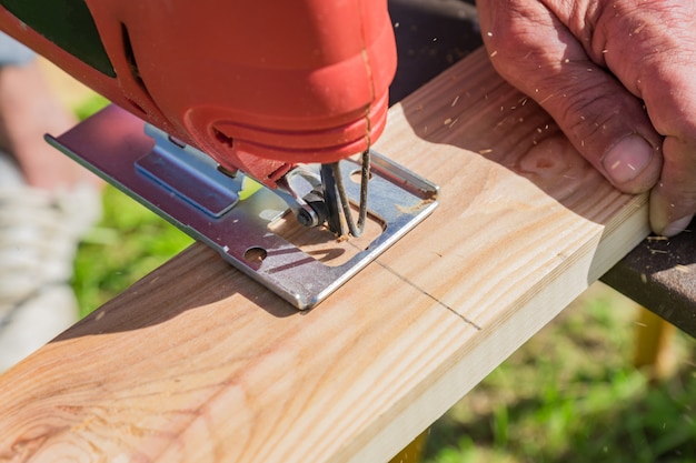 Wood worker cutting wooden panel with jig saw outdoors