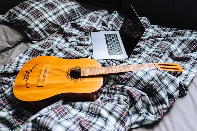 Wooden acoustic guitar on the bed with laptop.