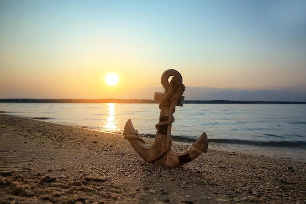 Photo wooden anchor on shore near river at sunset