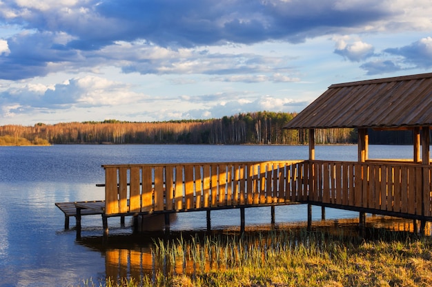春の湖の岸にある木製のアーバーと桟橋