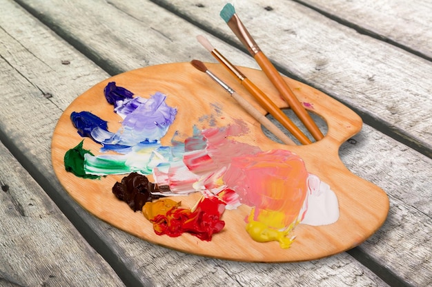 Wooden art palette with blobs of paint and  brushes on desk