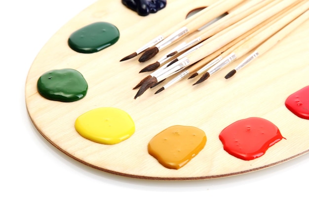 Photo wooden art palette with paint and brushes isolated on white