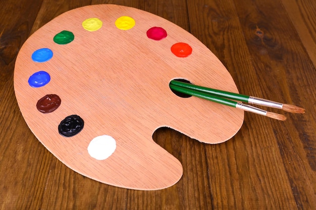 Wooden art palette with paint and brushes on table closeup