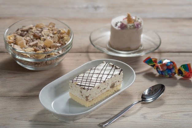 On a wooden background, bird's milk Cake with halva, chocolates and muesli in a plate. 