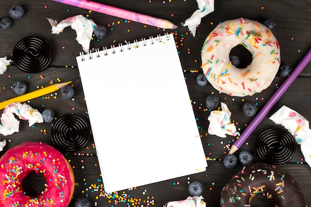 On a wooden background a blank notebook with a pencil colorful donuts and scraps of paper